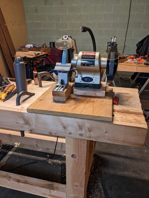 Bench grinder mounted on a board with the adjustable tool rest installed in front of it.